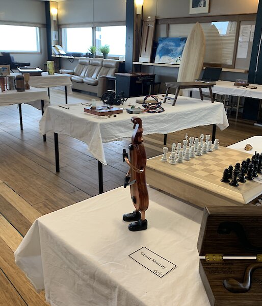A room with tables covered in white table cloths. Various hand made art items are displayed on the tables.