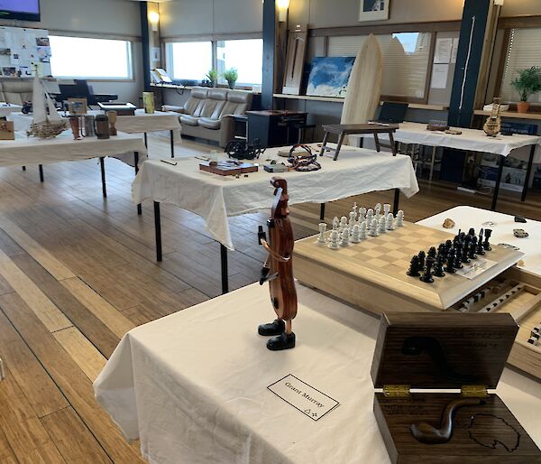 A room with tables covered in white table cloths. Various hand made art items are displayed on the tables.