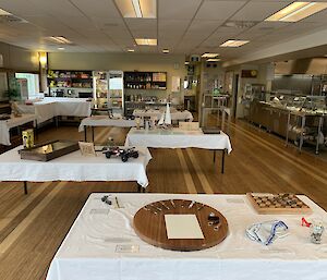 A room with tables covered in white table cloths. Various hand made art items are displayed on the tables.