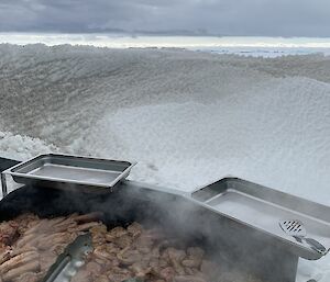 A BBQ full with cooking meat and onions against the snowy background