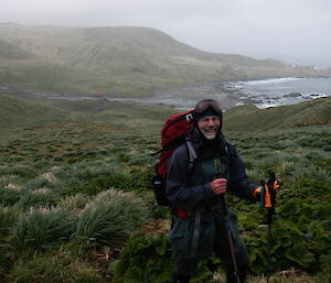 Mal standing in  the scrubby grass front of Bauer Bay in full hiking gear