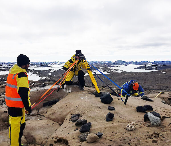 Photo of three men with some technical equipment with a rocky and slightly snow covered backdrop