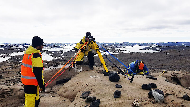 Photo of three men with some technical equipment with a rocky and slightly snow covered backdrop