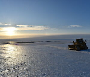 A tractor sits in the setting sun on an ice road