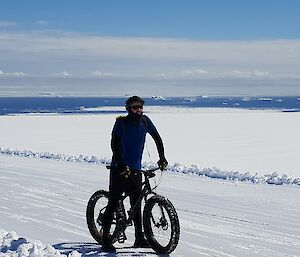 Expeditioner on pushbike. Icebergs on the ocean in the background.