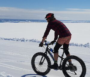 Expeditioner riding a pushbike on the snow. Ocean in the distance.