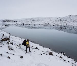 An expeditioner on a snowy bank looking across a lake