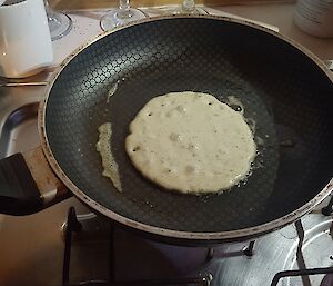 A frying pan with a half cooked pancake in the middle