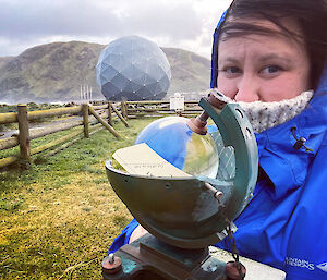 Alana standing next to a glass globe sunshine recorder, with the ANARE satellite in the background