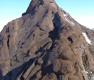 The steep , rocky peak of a mountain against the sky