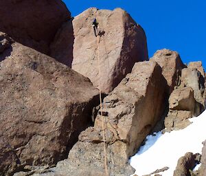 Looking up towards a climber abseiling down a rocky mountain