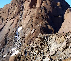 Climbers, attached to ropes, traverse across some smaller rocks and crumbling choss