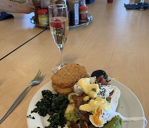 A plate of eggs Benedict with a flute of Champagne