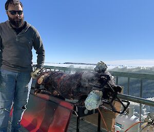 An expeditioner stands by the BBQ, snow in the background.  A whole pig is roasting on a spit