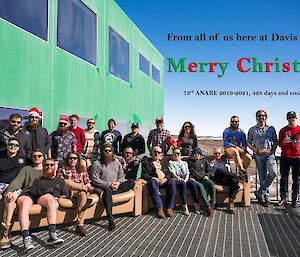 Expeditioners in a group photo on the outside deck, some with Santa hats on.  Text on photo reads 'From all of us here at Davis station, Merry Christmas.  73rd Anare 2019-20, 428 days and counting