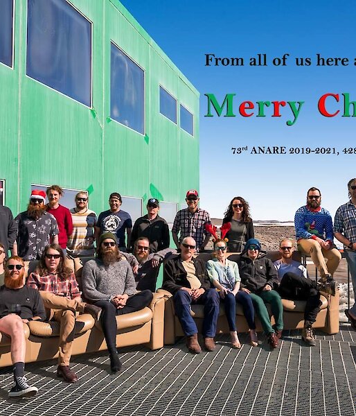 Expeditioners in a group photo on the outside deck, some with Santa hats on.  Text on photo reads 'From all of us here at Davis station, Merry Christmas.  73rd Anare 2019-20, 428 days and counting