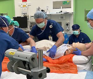 Group of people in surgical scrubs with a dummy patient on a hospital operating table