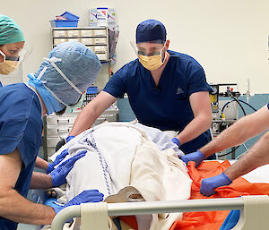 Doctor and assistants, wearing masks and scrubs, with a dummy patient in a hospital operating theatre