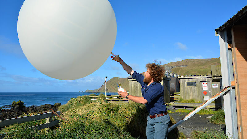 Man in casual clothes releasing a large white balloon near a grassy beach