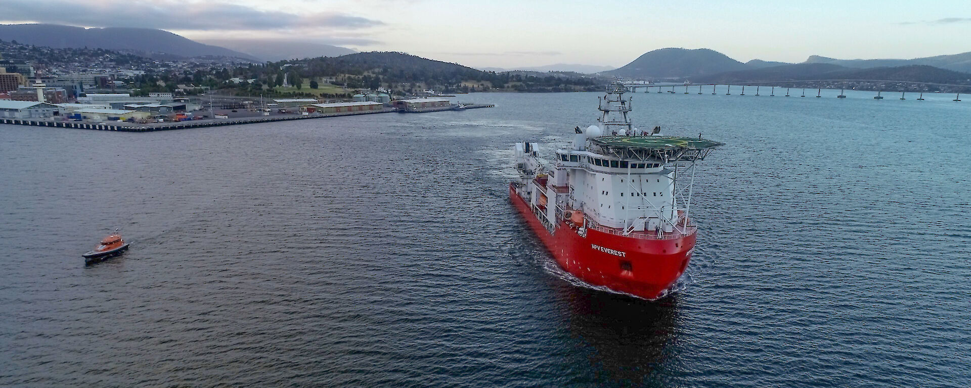 giant ship with pilot heads down river from city