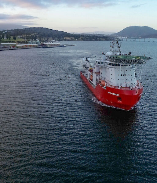 giant ship with pilot heads down river from city