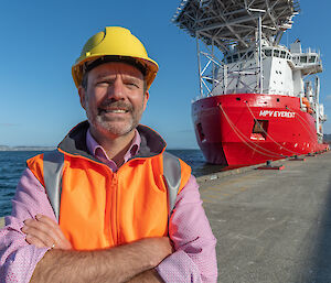 man in hi-vis and hard hat with giant ship in background