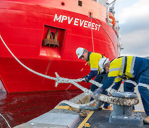 two men handle a rope attached to wharf and ship