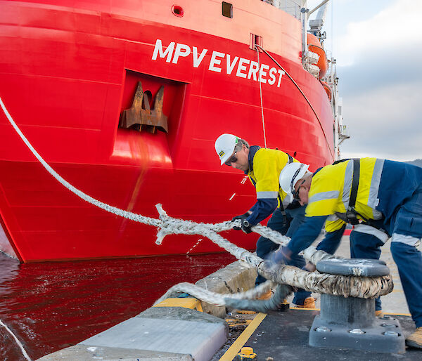 two men handle a rope attached to wharf and ship