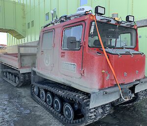 A red Hagglund covered in dust parked outside a green shed
