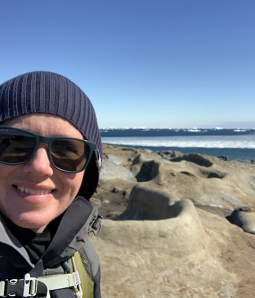 Selfie of expeditioner in beanie and sunglasses with ellie seal in the background