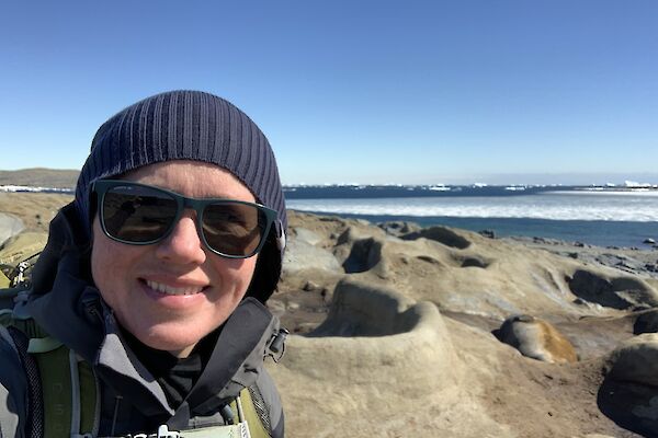 Selfie of expeditioner in beanie and sunglasses with ellie seal in the background