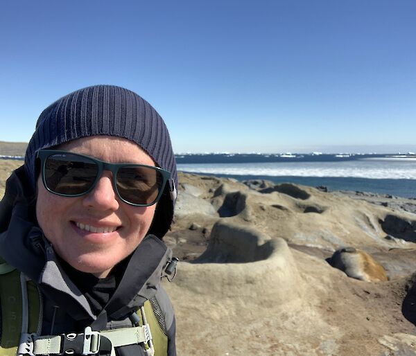 Selfie of expeditioner in beanie and sunglasses with ellie seal in the background