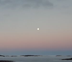 A pastel sunset with the moon in the middle of shot