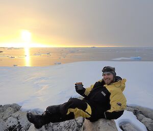 Man reclines on an icy rock near the ocean.