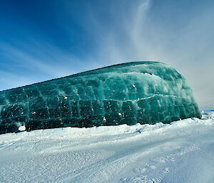 A glorious fully jade iceberg against the snow and blue skies