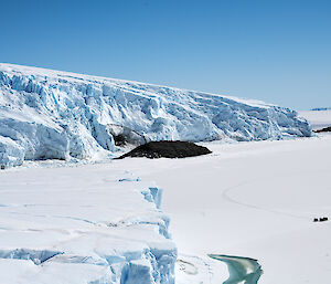 Large grounded iceberg encased in sea ice taken from above.  Three tiny Hagglunds can be seen parked on the ice in the distance.