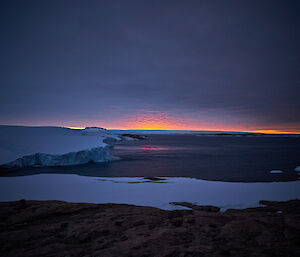 A orange and pink sunset peeping out from the bottom of the clouds on the horizon.