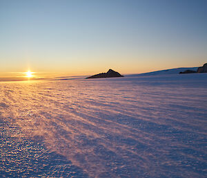 A large expanse of snowy ground leading off towards a setting sun in the distance