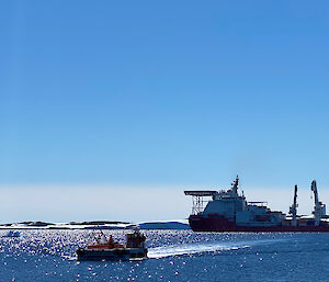 A small boat heads towards a bigger boat in the bay.  Snowy landscape on the horizon.