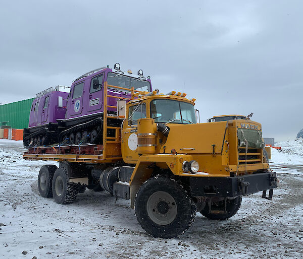 Purple Hägglunds vehicle on the back of a Mack truck.