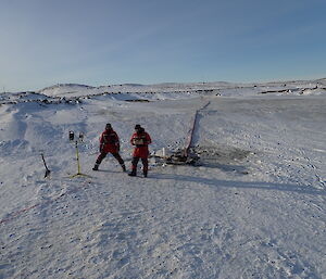 Two expeditioners standing on the frozen water with pipes and equipment