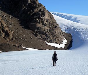 An expeditioner walks away from camera towards a mountain surrounded by a wind scour