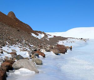 An expeditoner walking away from camer on the frozen lake Mount Burnett visible