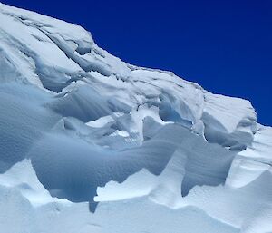 A large snow cornice (an overhanging edge of snow on a ridge or mountain) against a bright blue sky
