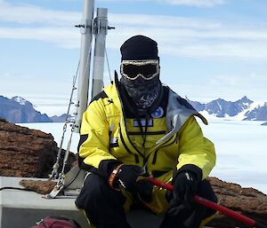 An expeditioner sits looking to camera with his full hiking gear on including snow goggles, beanie and scarf