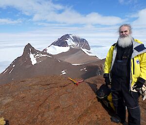 Expeditioner stands at the peak of the mountain with the ridge in the background and surrounded by ice