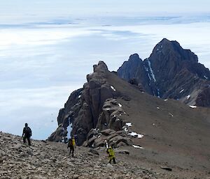 Three expeditioners carefully descending Mt. Parsons down the rocky ridge with ice below all around