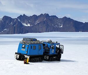 A blue Hagglund sitting on the ice with mountains in the background