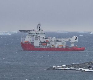 A red supply ship sailing away from the land with icebergs in the distance