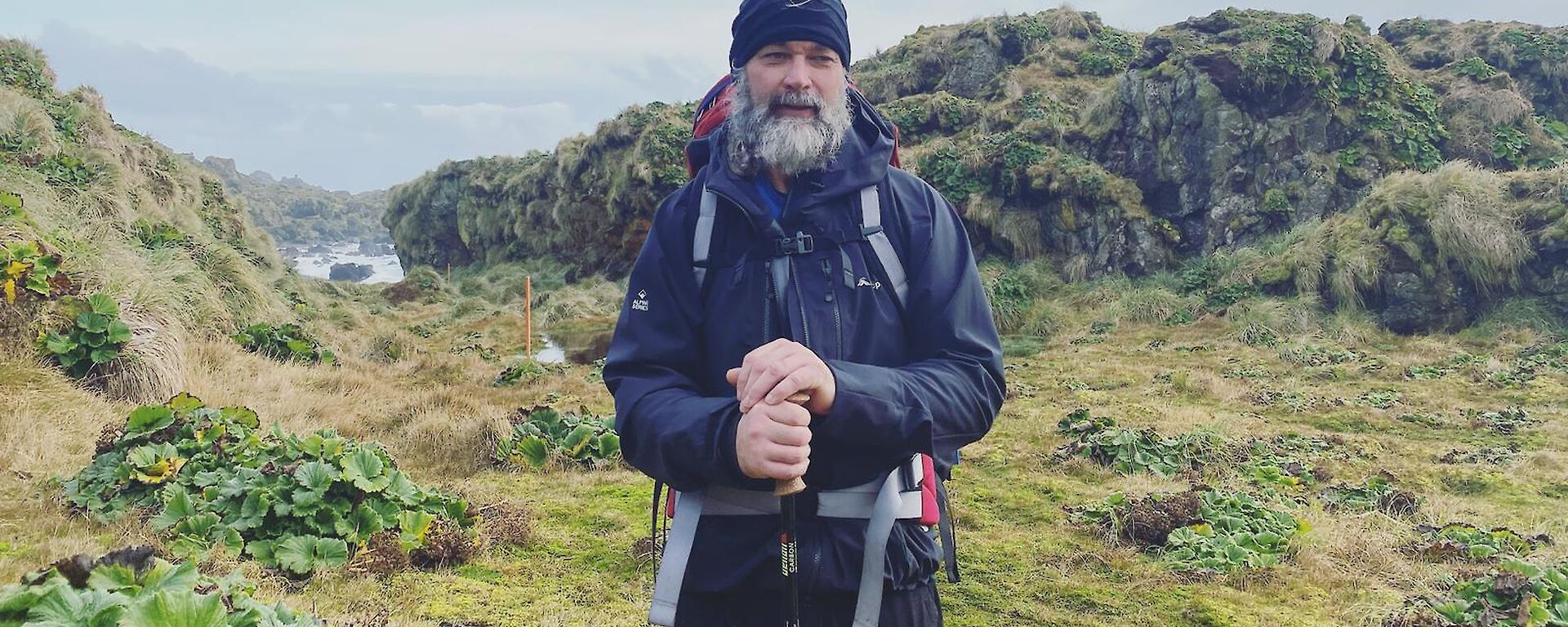 Expeditioner standing at the top of a hill in his hiking gear, smiling to camera